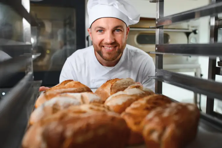 male-baker-smiling-with-fresh-bread-in-rack.jpg