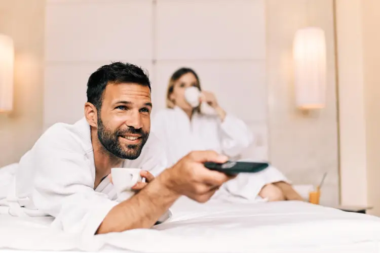 man-watching-tv-hotel-bed-coffee-mug.jpg